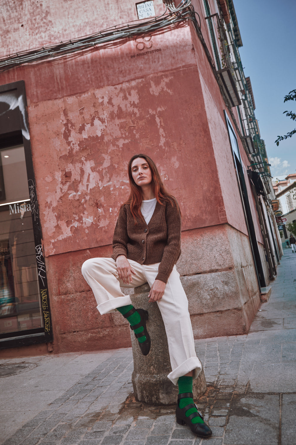 Woman sitting on a wall in an urban setting with a pink building in the background