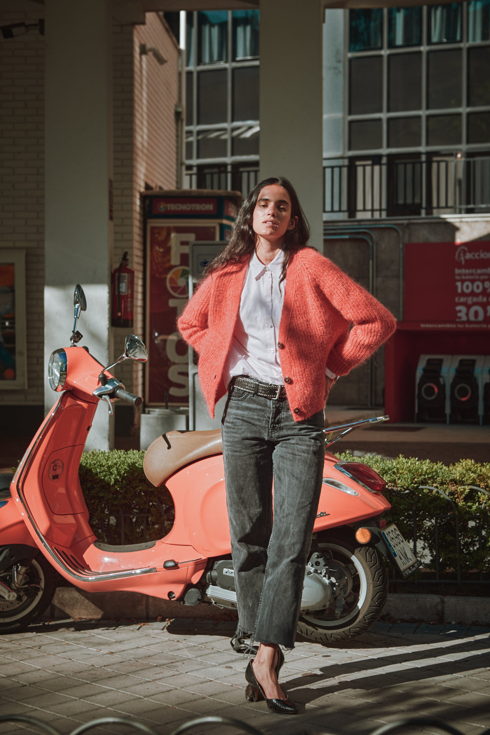 Woman in a red coat standing next to a red scooter in an urban setting