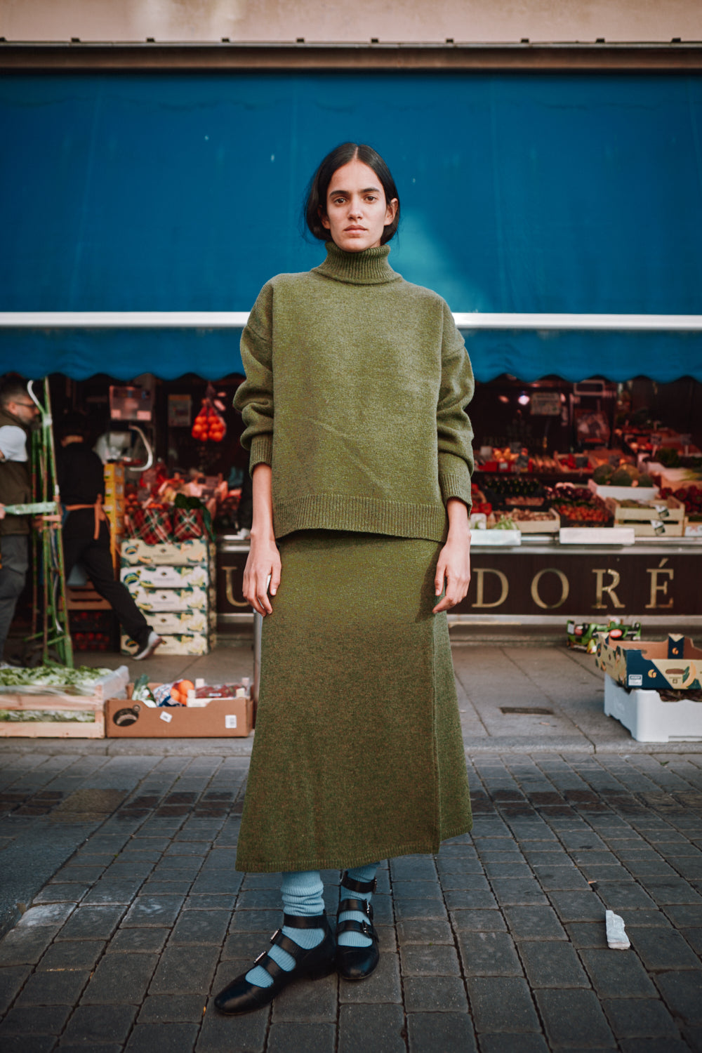 Person wearing a green outfit standing in front of a market stall