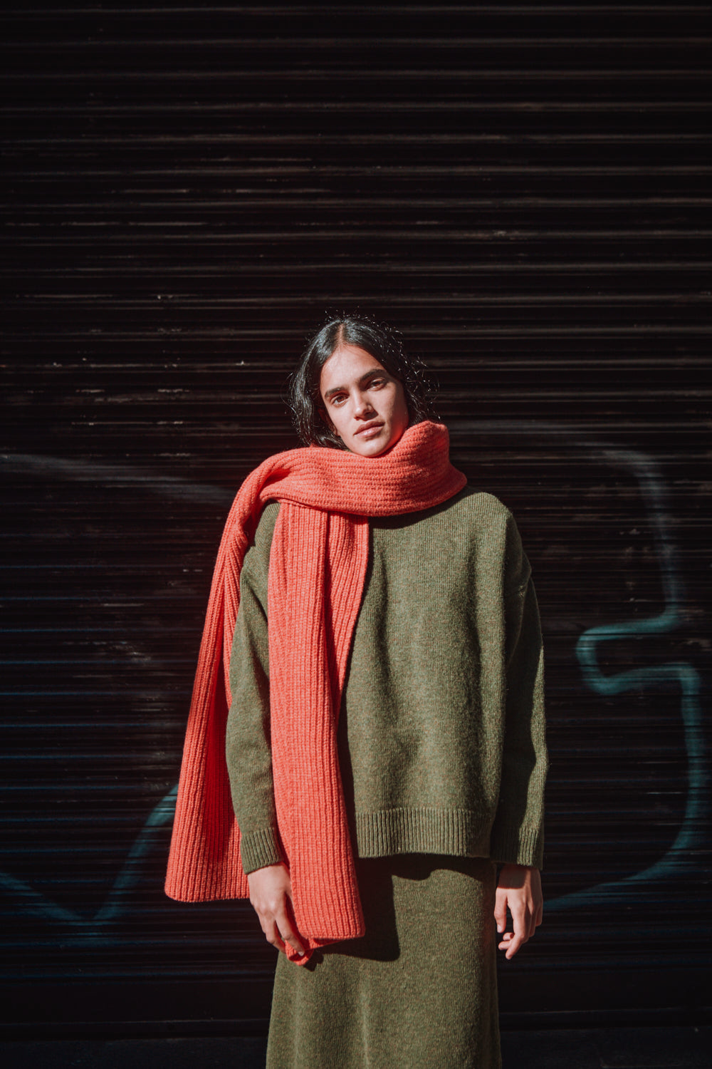 Person wearing a green sweater and coral scarf against a dark background