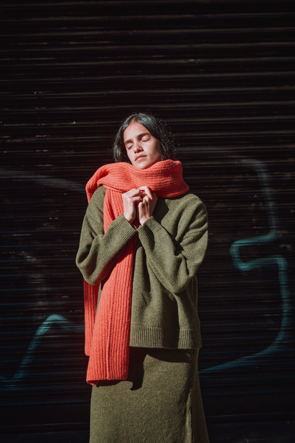 Person wearing a green sweater and coral scarf against a dark background