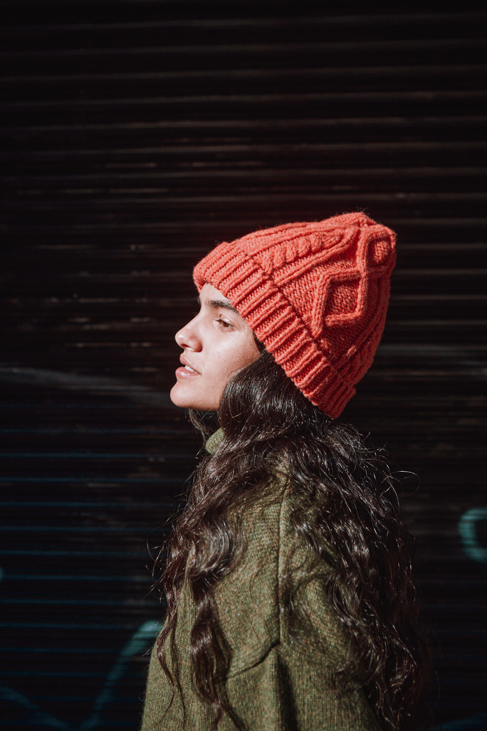 Woman wearing a coral knitted beanie against a dark background
