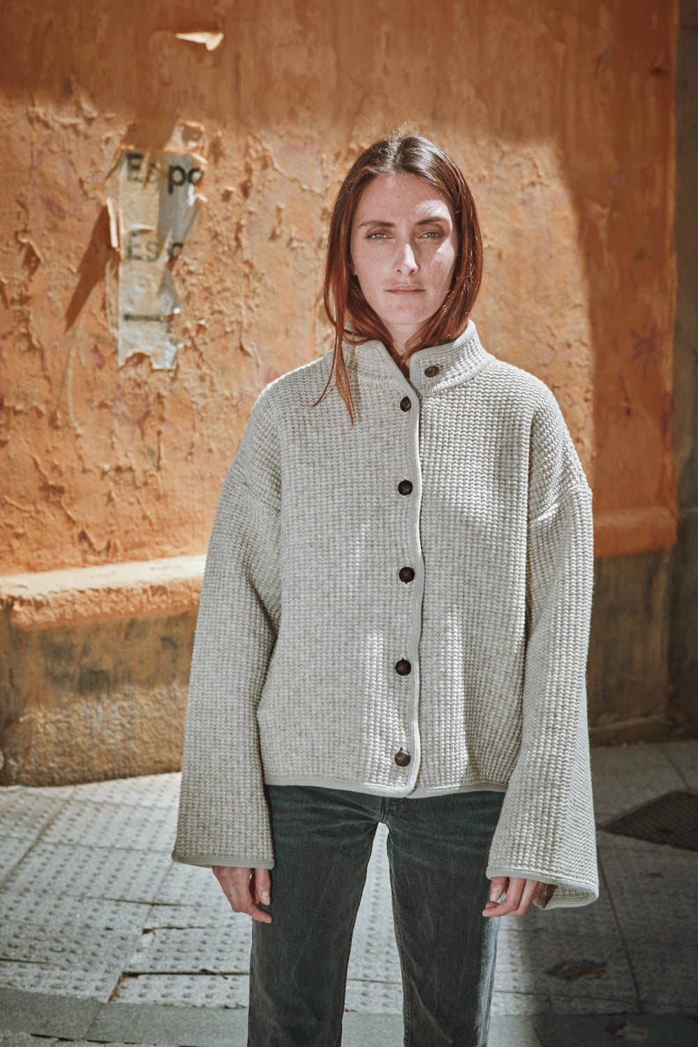 Person wearing a textured gray jacket standing against a textured wall.