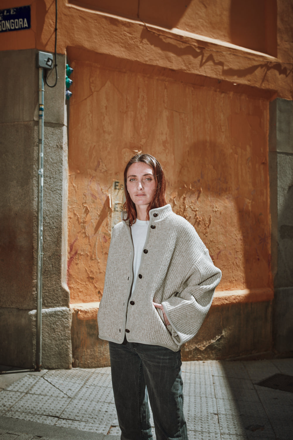 Person wearing a light gray coat standing against a textured wall.