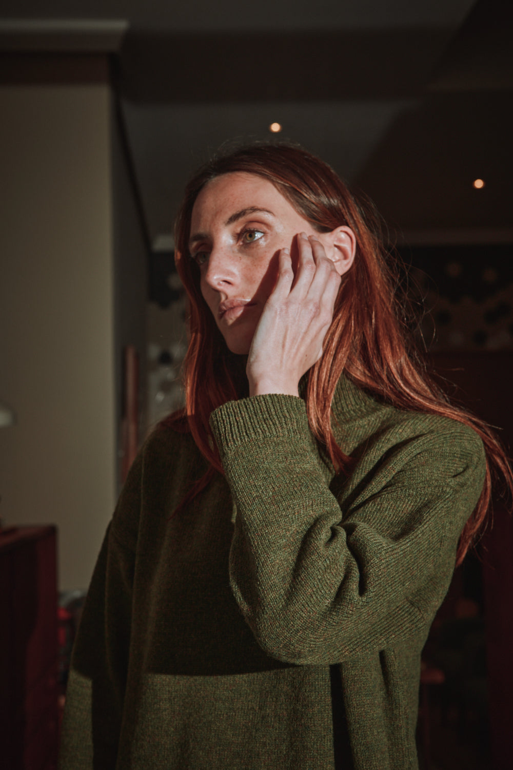 Woman in a green dress touching her face in a dimly lit room