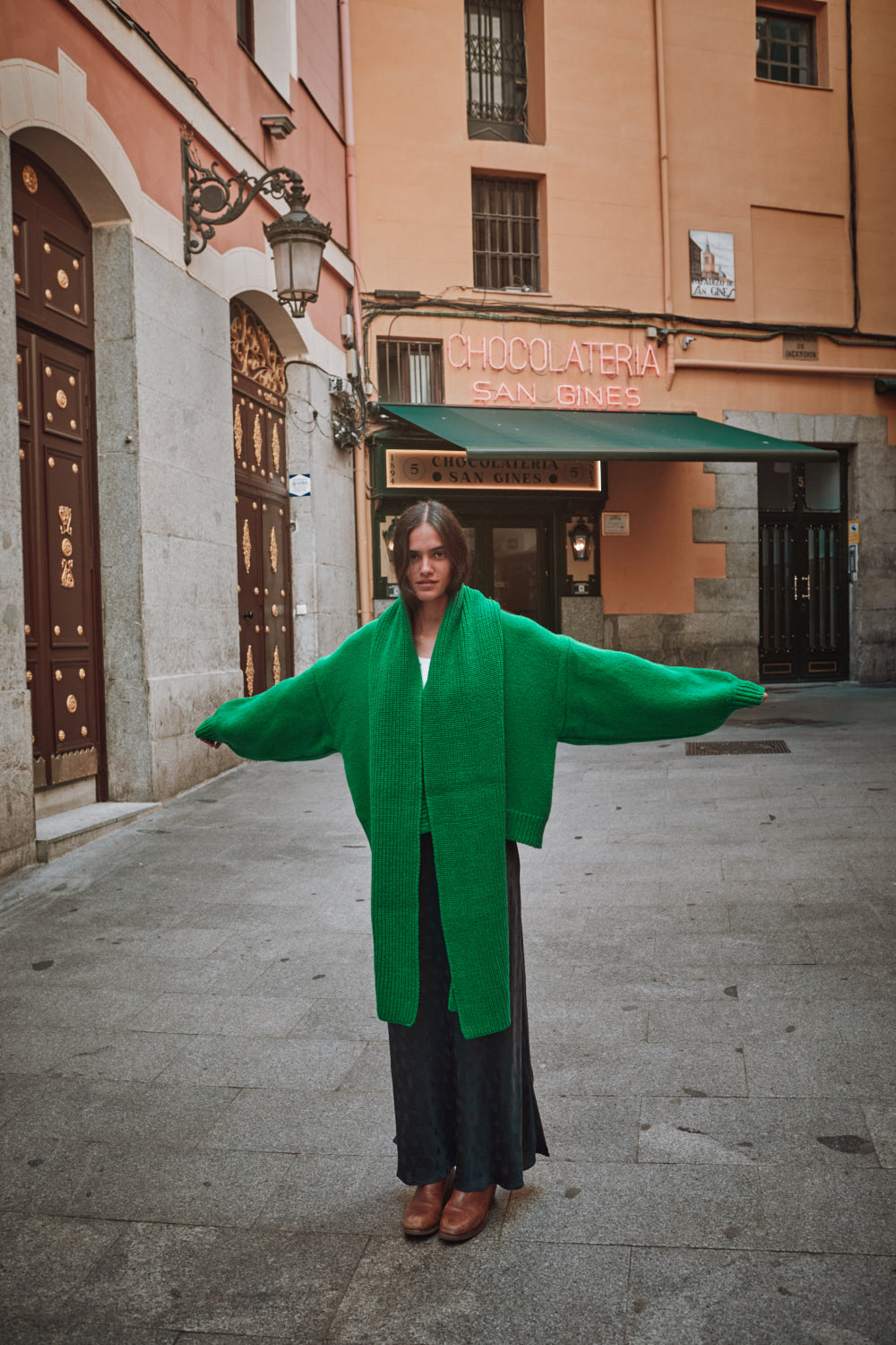 Person wearing a green coat standing on a street with buildings in the background