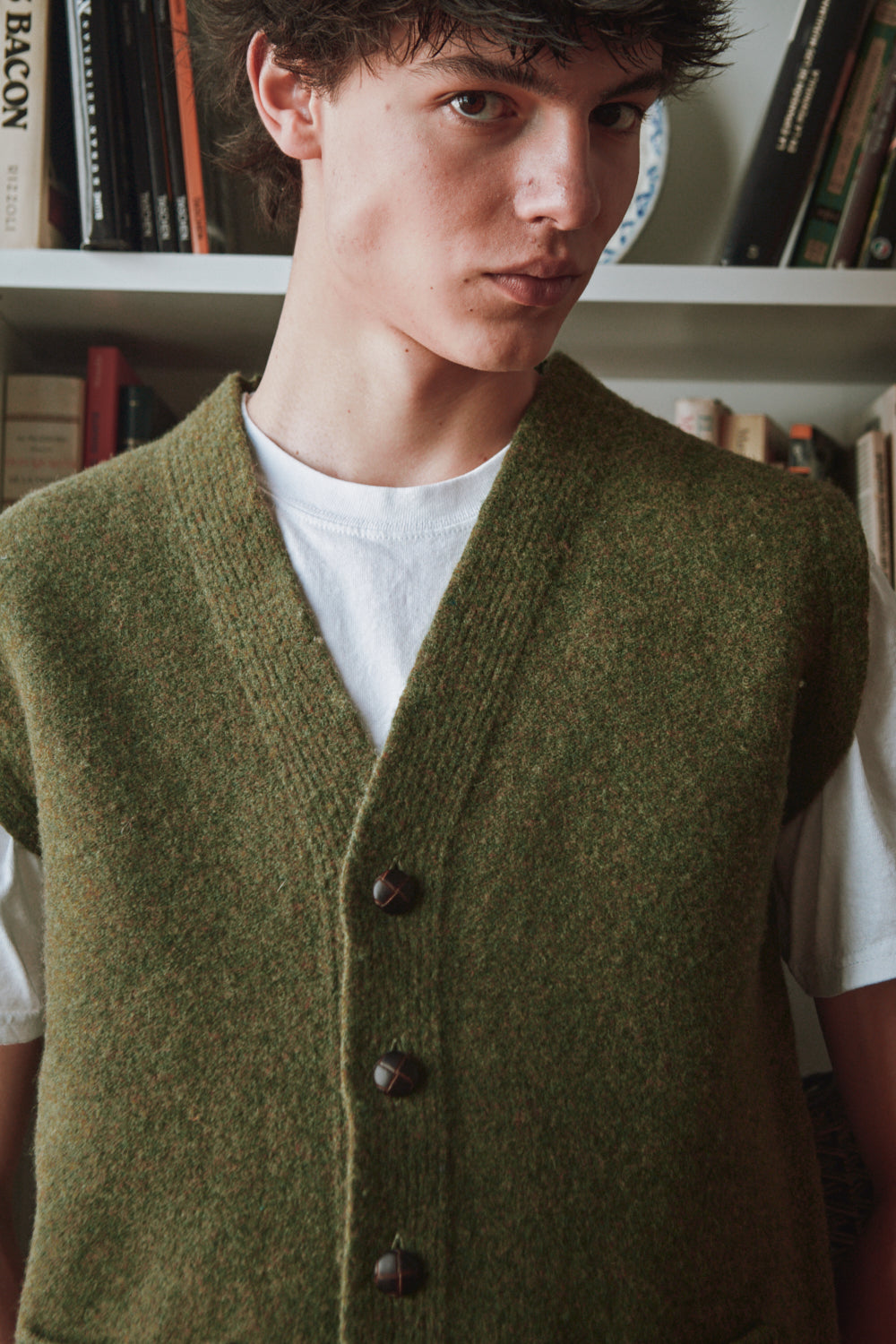 Homme portant un gilet vert sur une chemise blanche avec une bibliothèque en arrière-plan