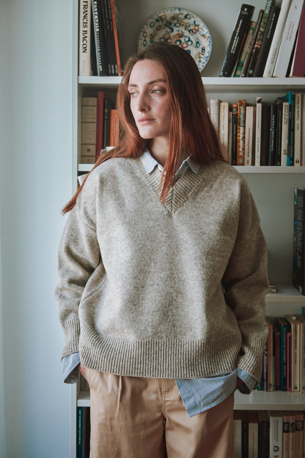 Personne portant un pull beige dans une pièce avec des étagères.