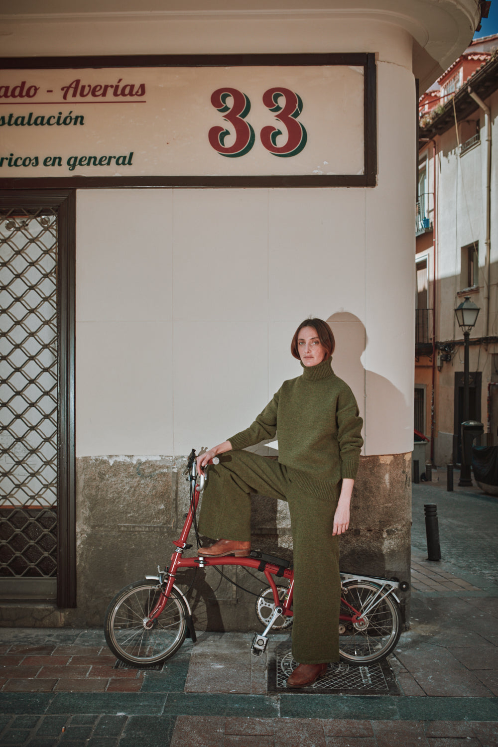 Personne en gilet et pantalon verts avec une bicyclette rouge contre un bâtiment