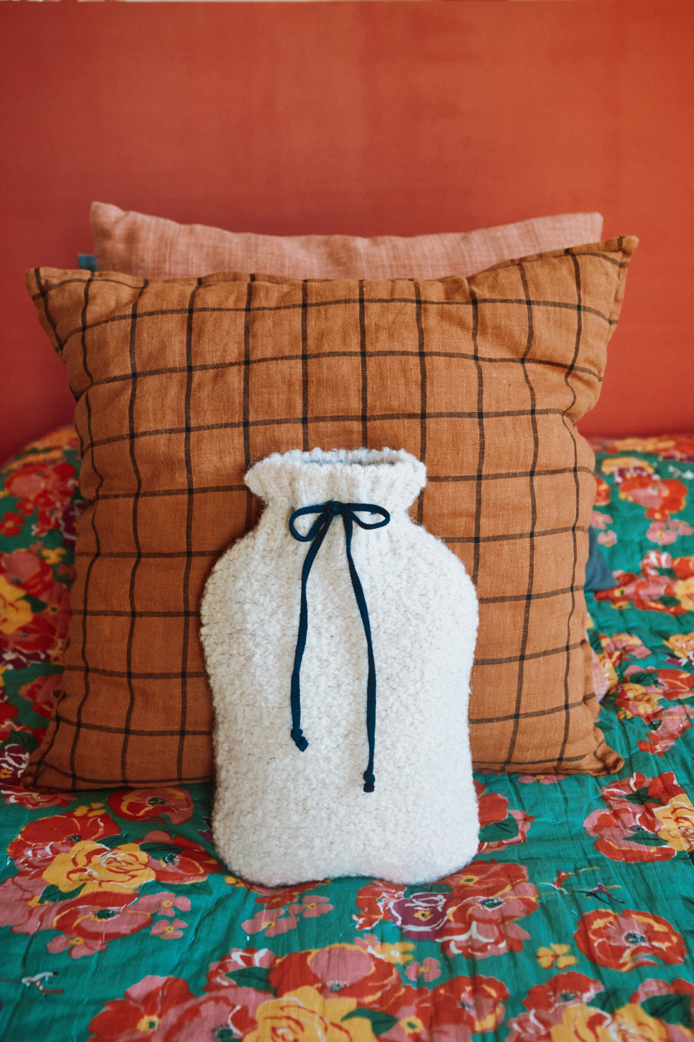 White hot water bottle with a blue drawstring on a couch with an orange checkered pillow.