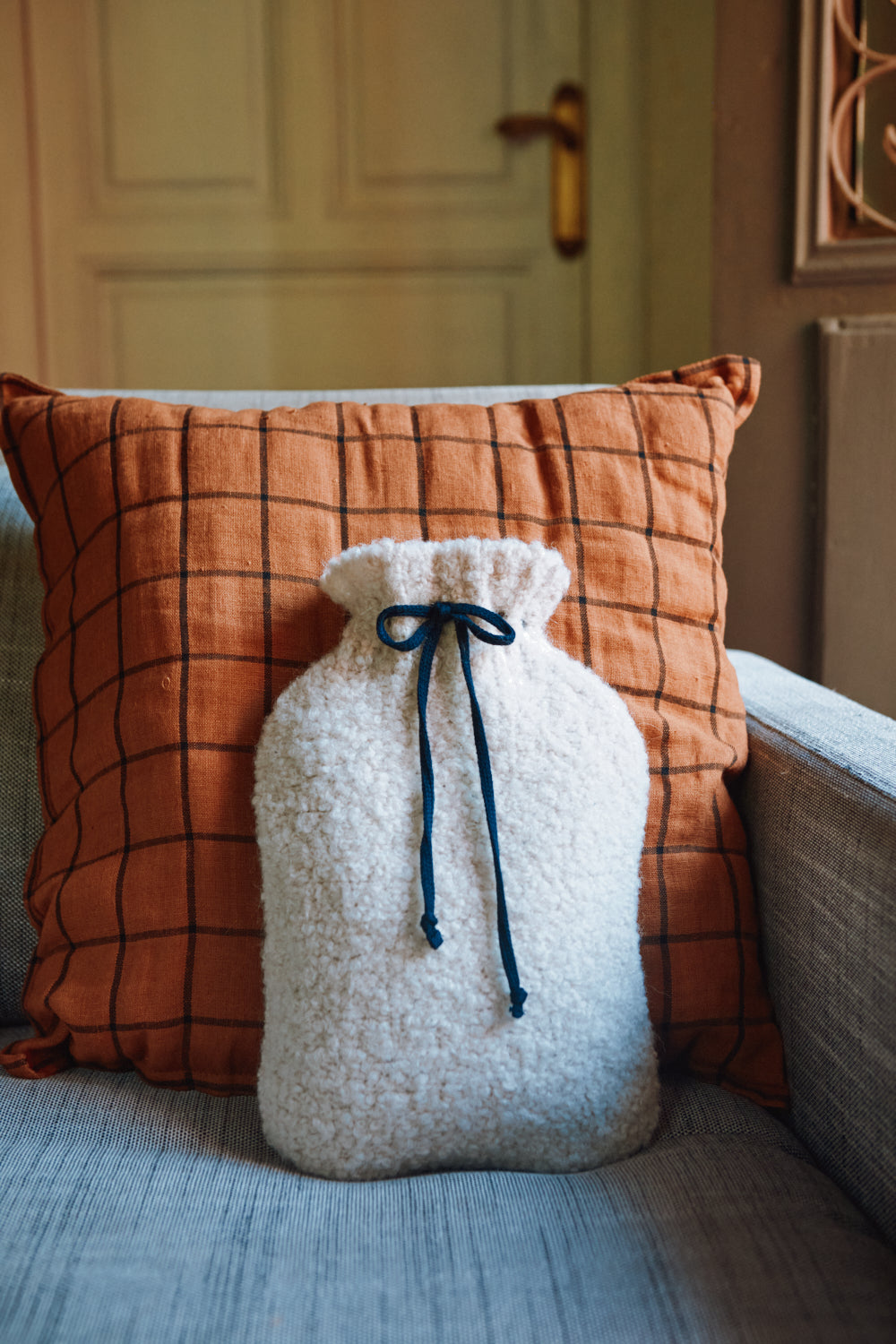 White hot water bottle with a blue drawstring on a couch with an orange checkered pillow.