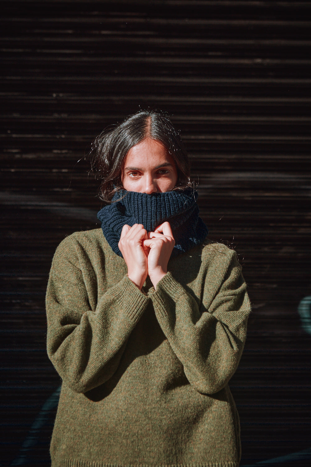 Person wearing a green sweater and blue knitted scarf against a dark background
