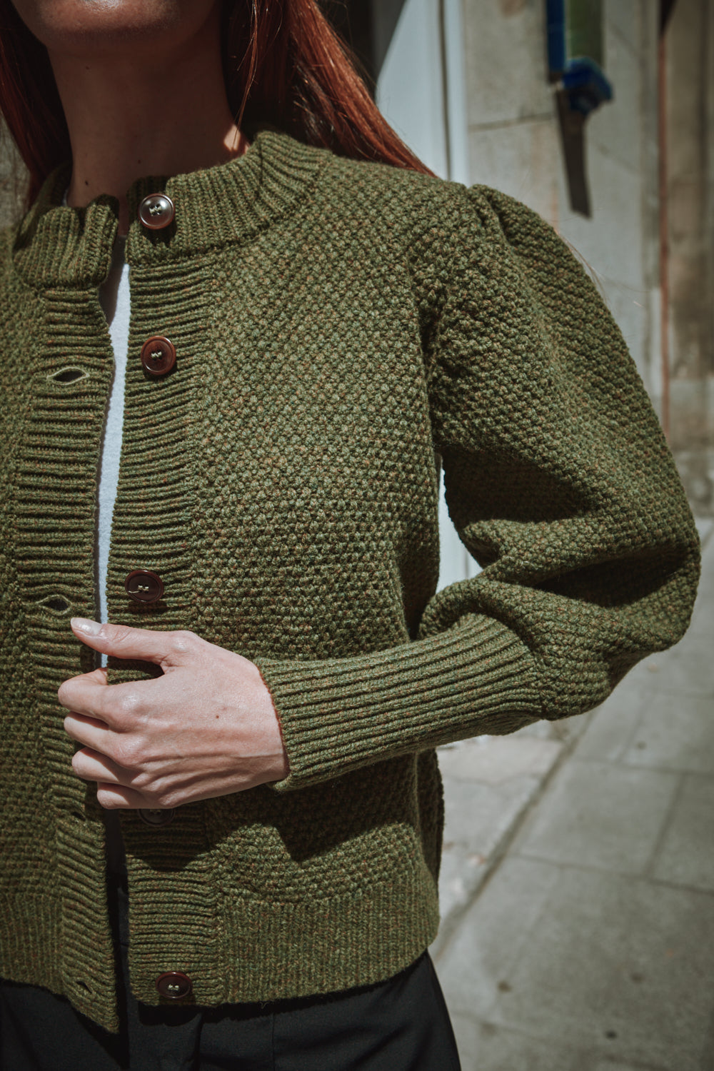Woman wearing a green L'ENVERS cardigan standing in front of a building with a decorative emblem.