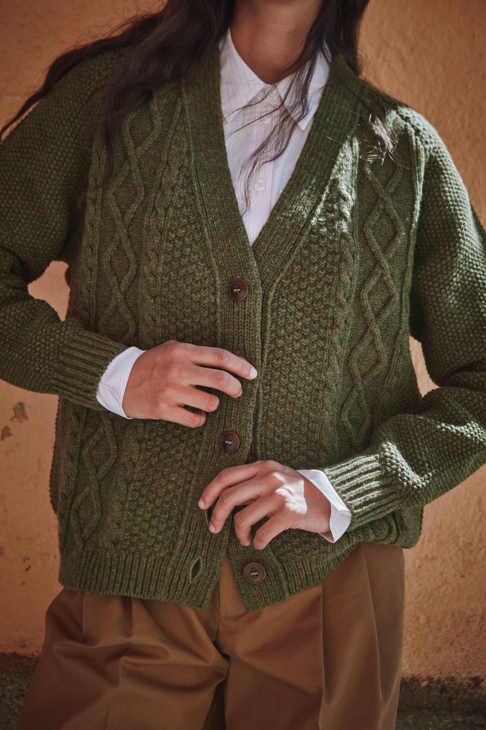 Person wearing a green knitted cardigan with a textured pattern against a warm-toned background