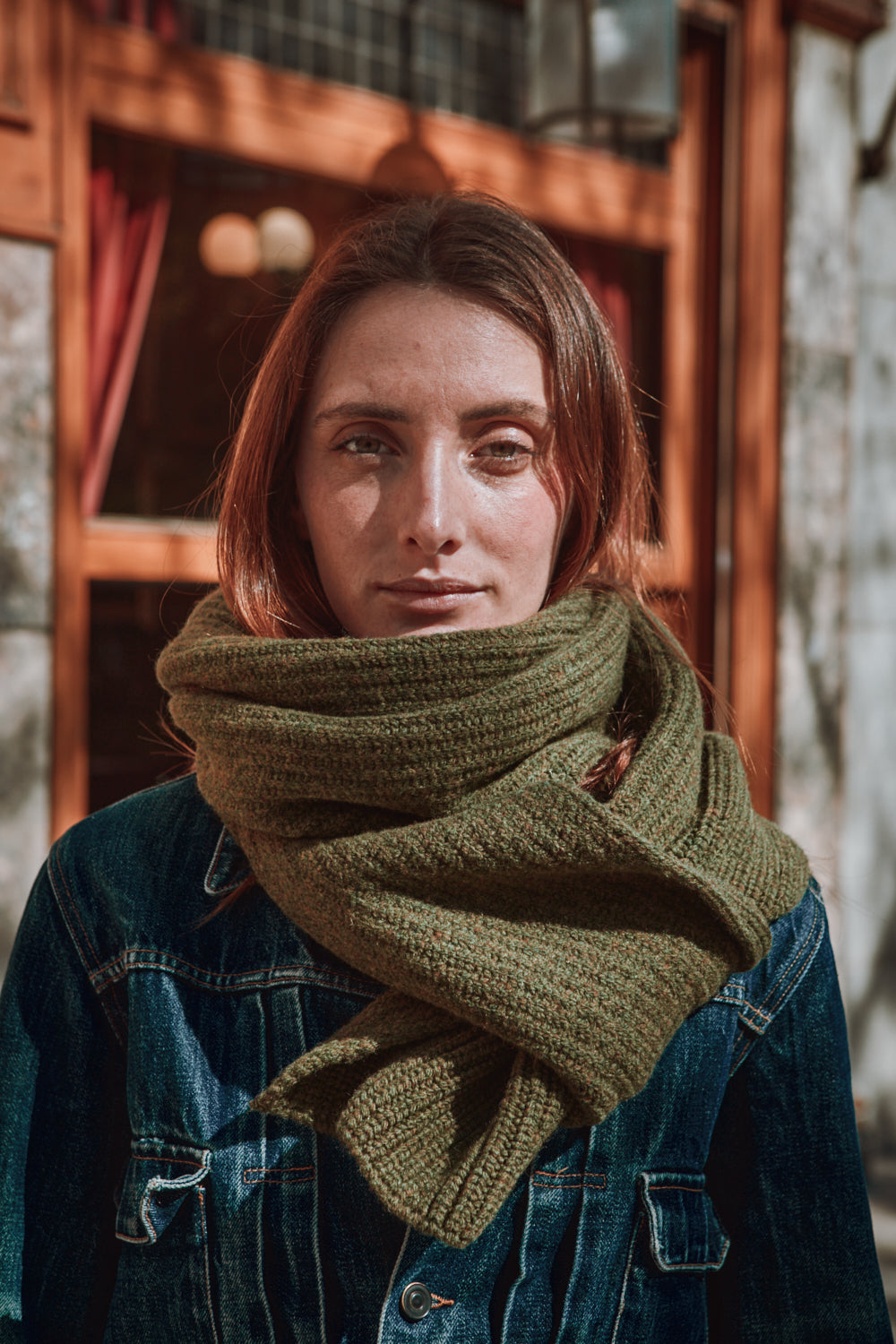 Woman wearing a green knitted scarf in front of a wooden building.