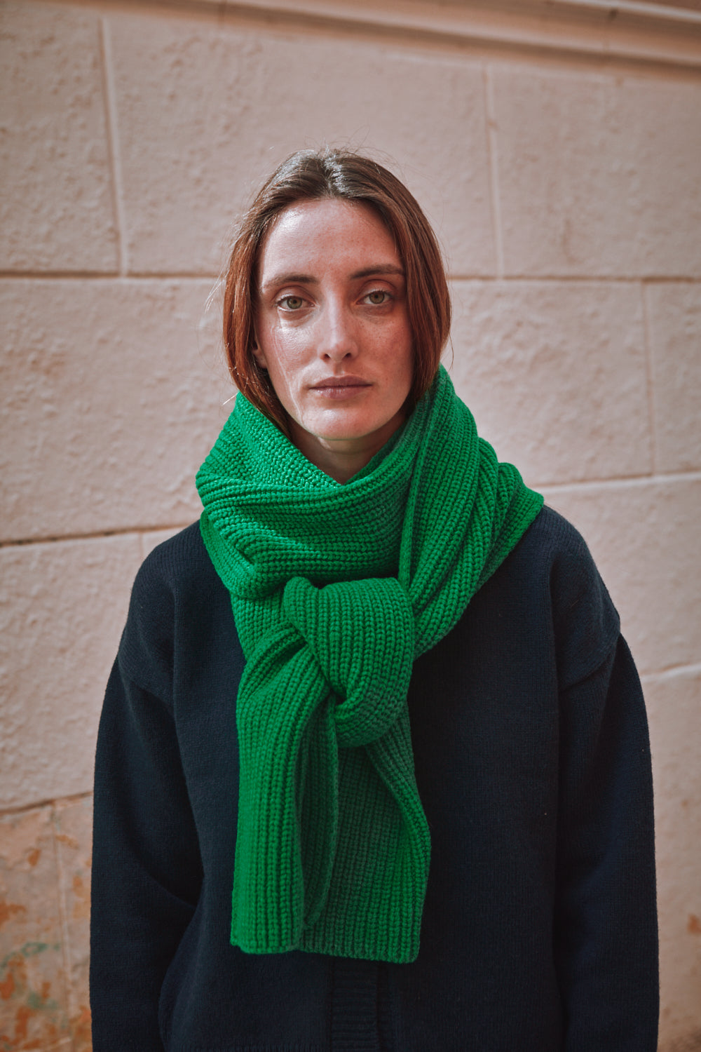 Person wearing a green scarf against a stone wall background