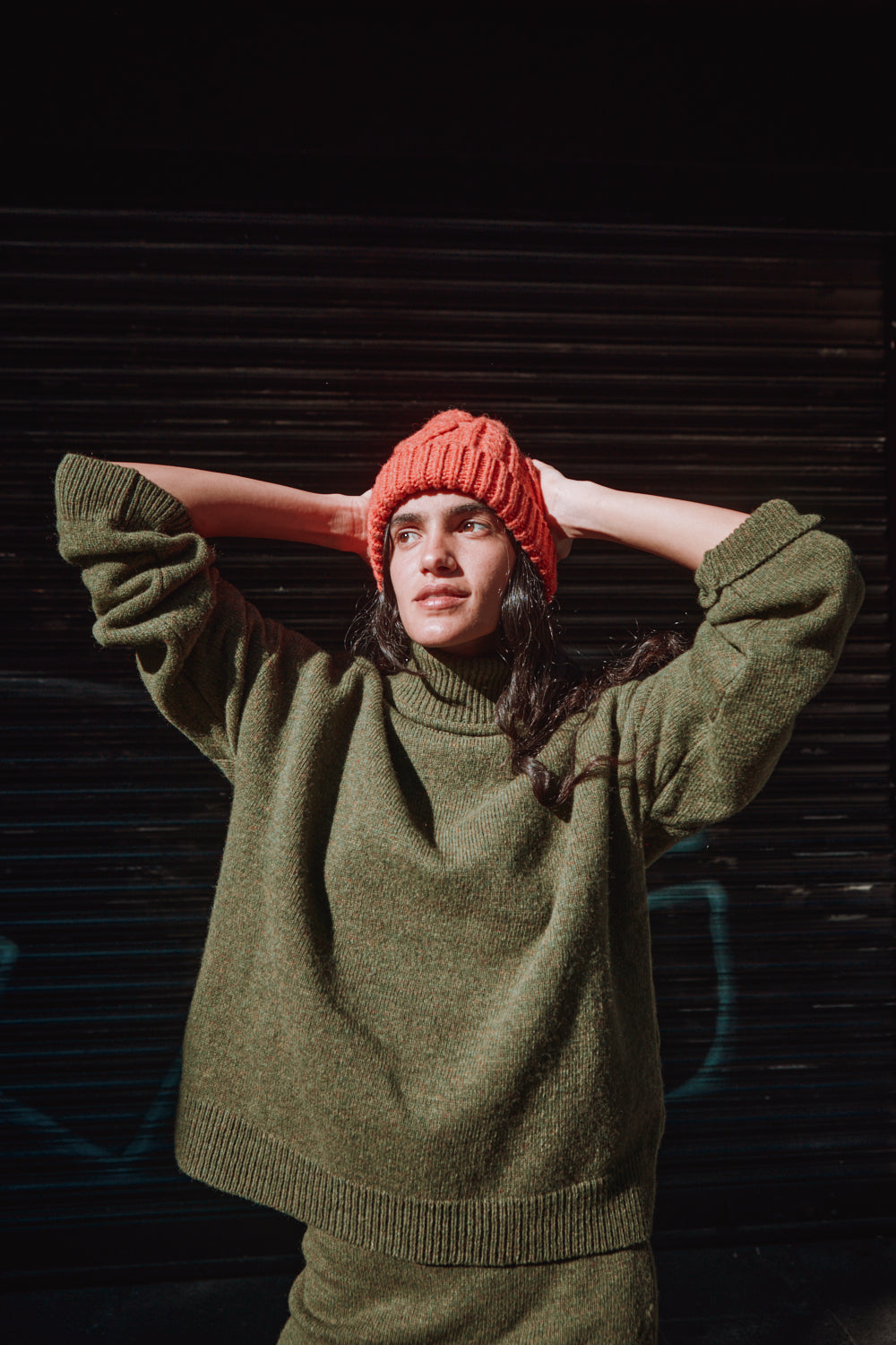 Person wearing a green sweater and red beanie against a dark background