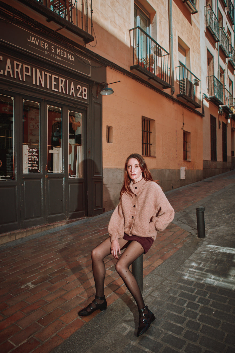 Woman sitting on a bench in front of a building with 'Carpinteria 28' sign.