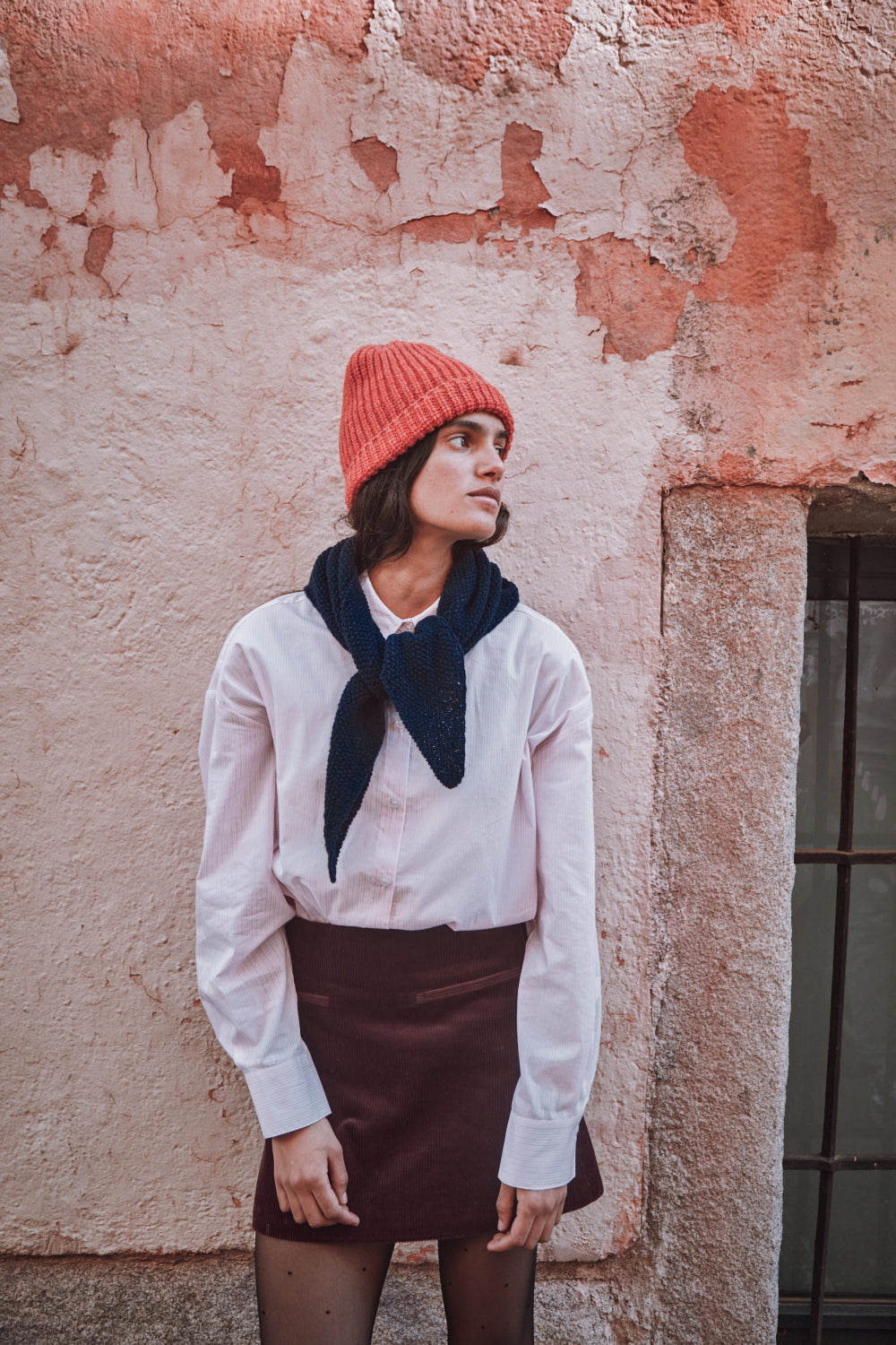 Person wearing a pink beanie and dark scarf against a textured wall.