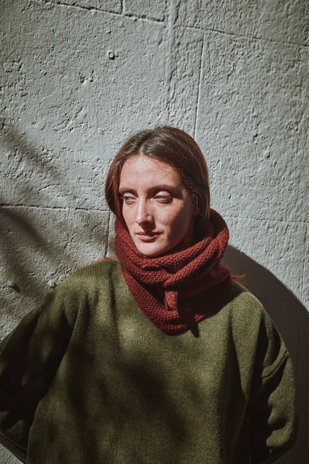Person wearing a green sweater and red scarf against a textured wall