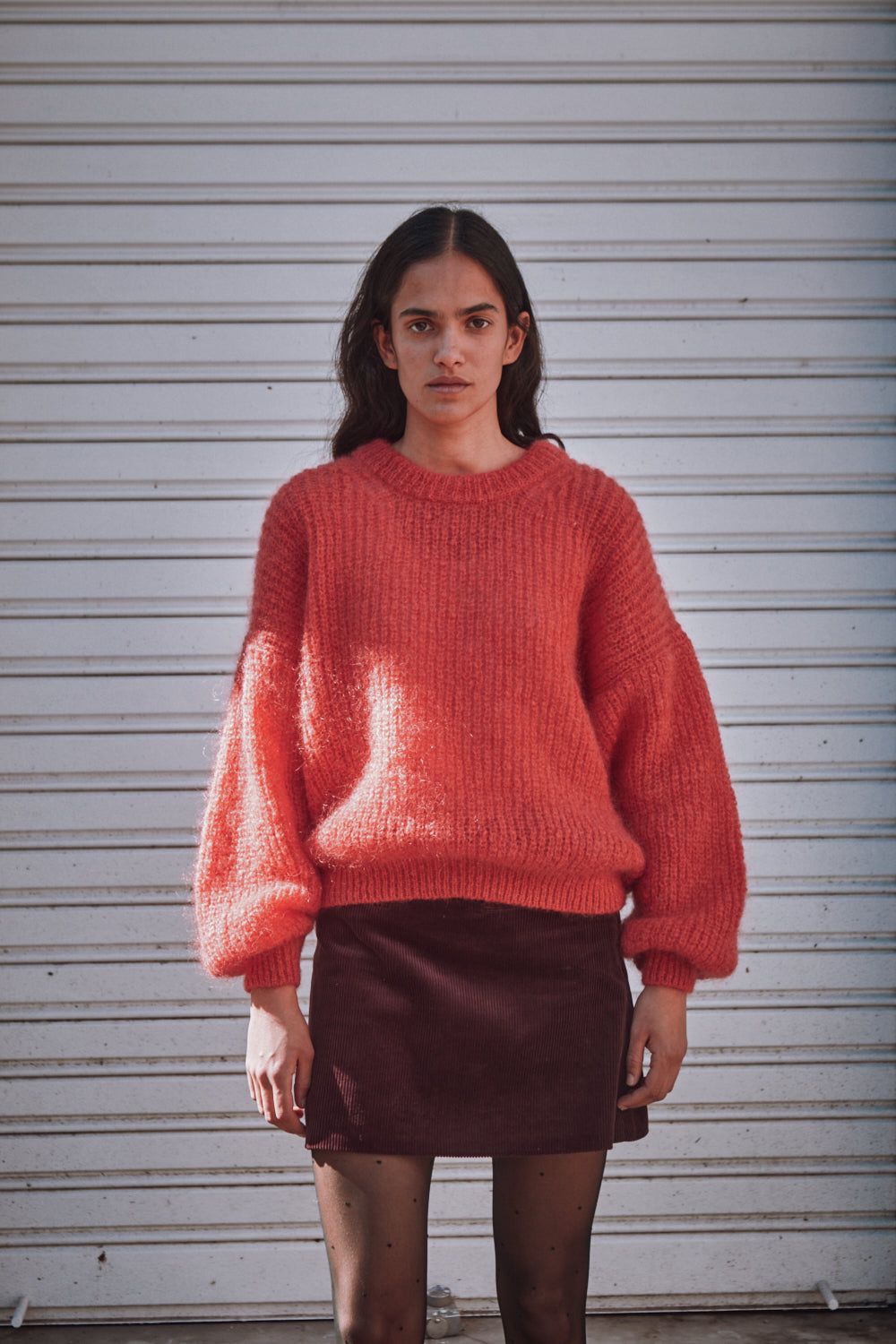 Woman wearing a red sweater and brown skirt against a white wall