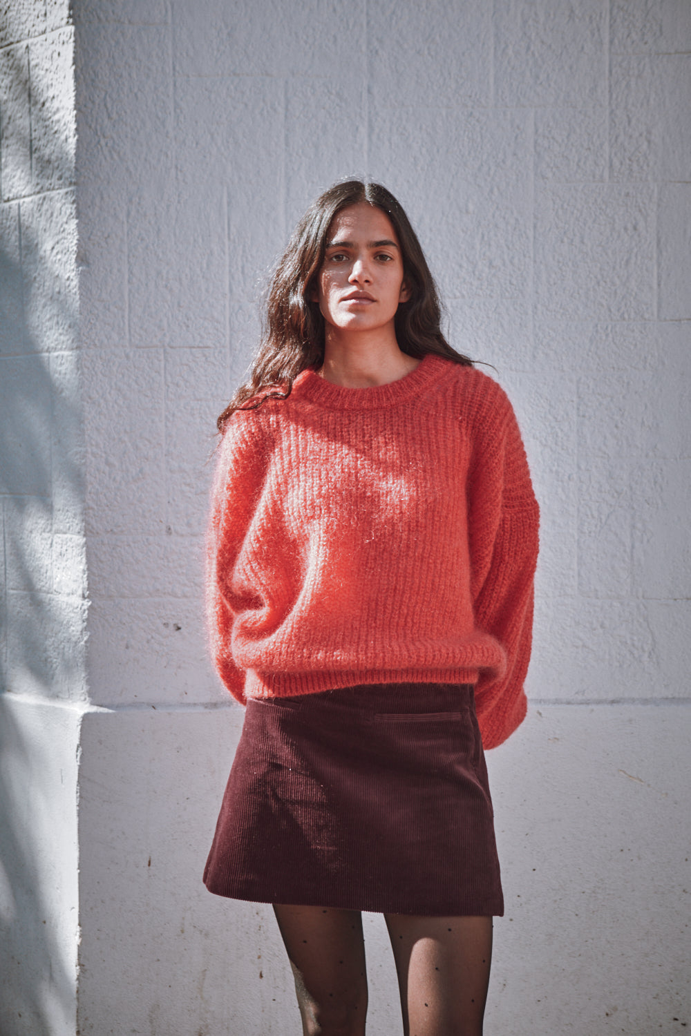 Woman wearing a red sweater and brown skirt against a white wall