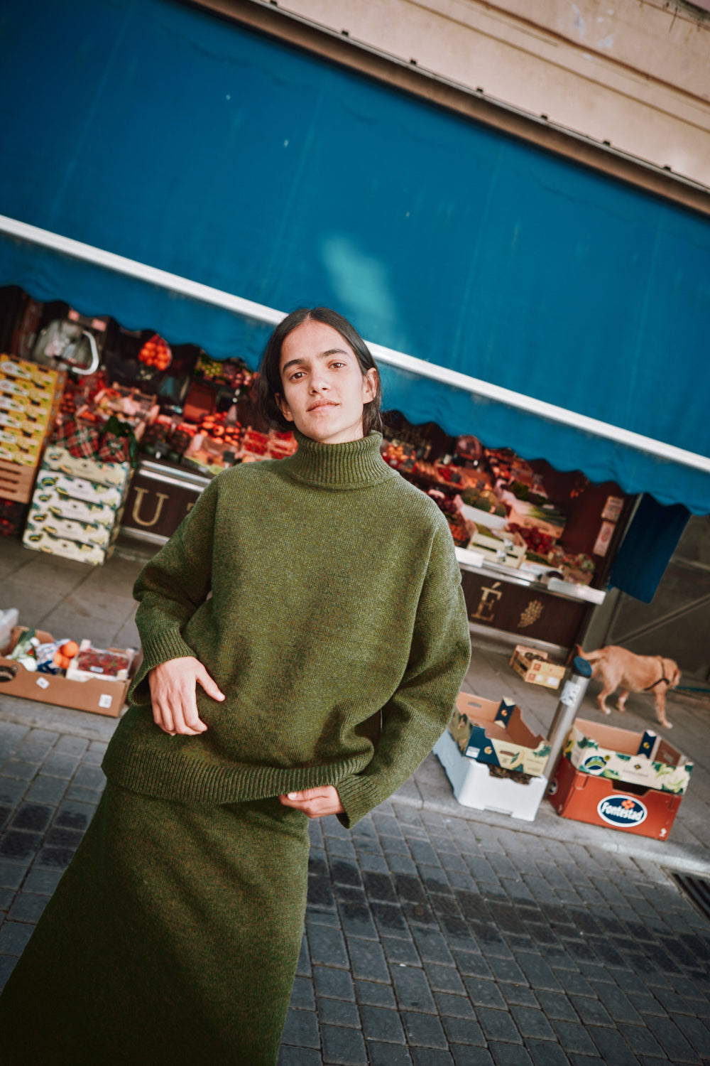 Person wearing a green L'ENVERS outfit standing in front of a market