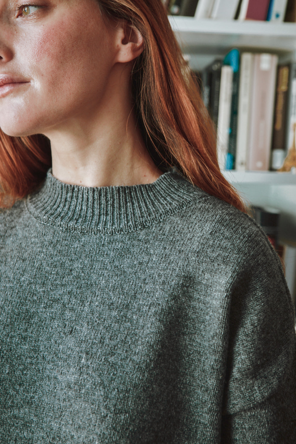 Person wearing a grey dress with a blurred background of books on a shelf