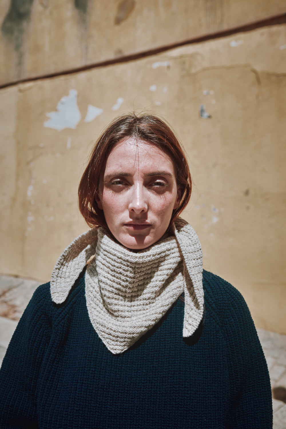 Woman wearing a textured beige scarf against a textured wall