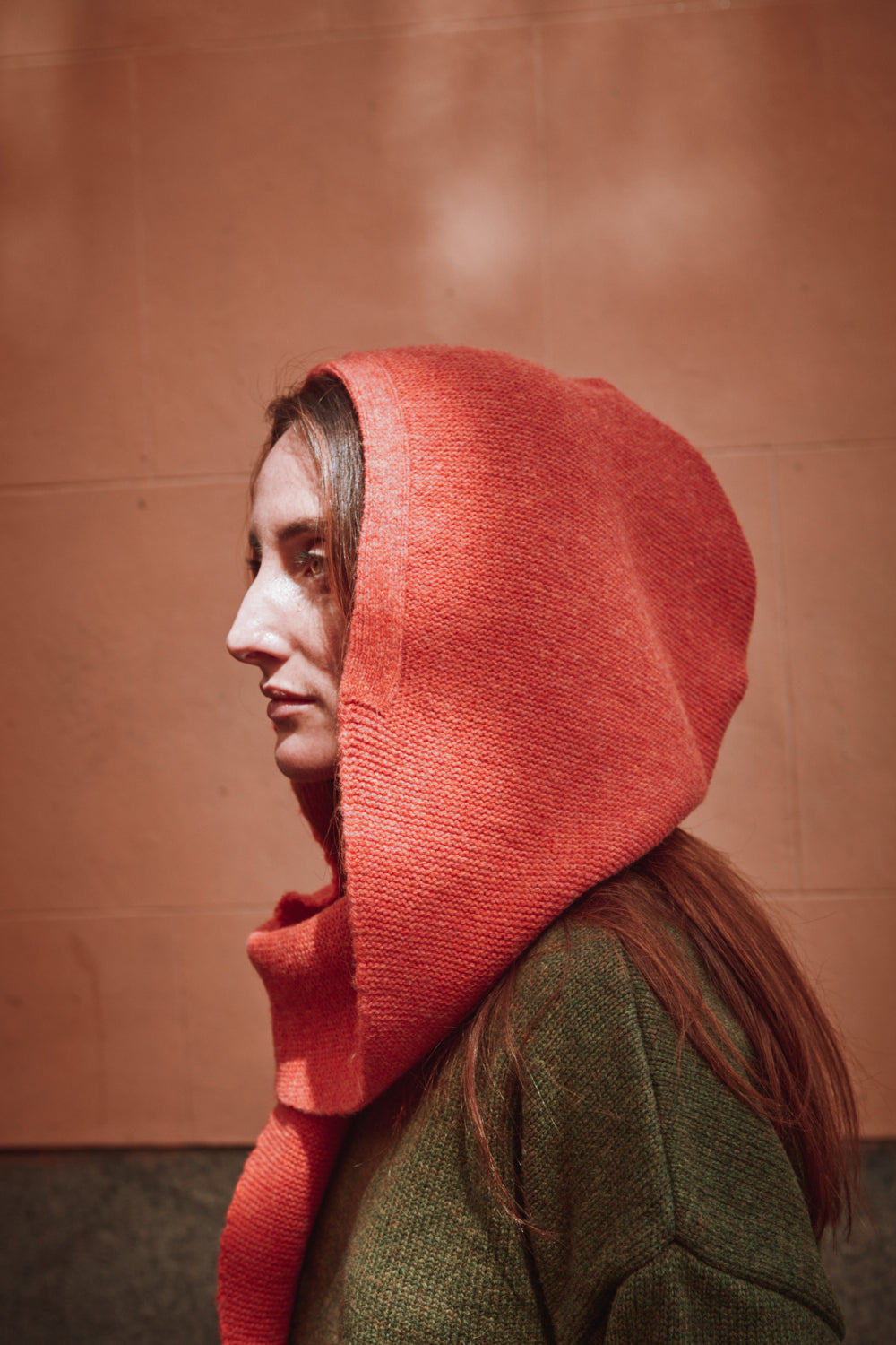 Person wearing a coral hooded garment against a brown background