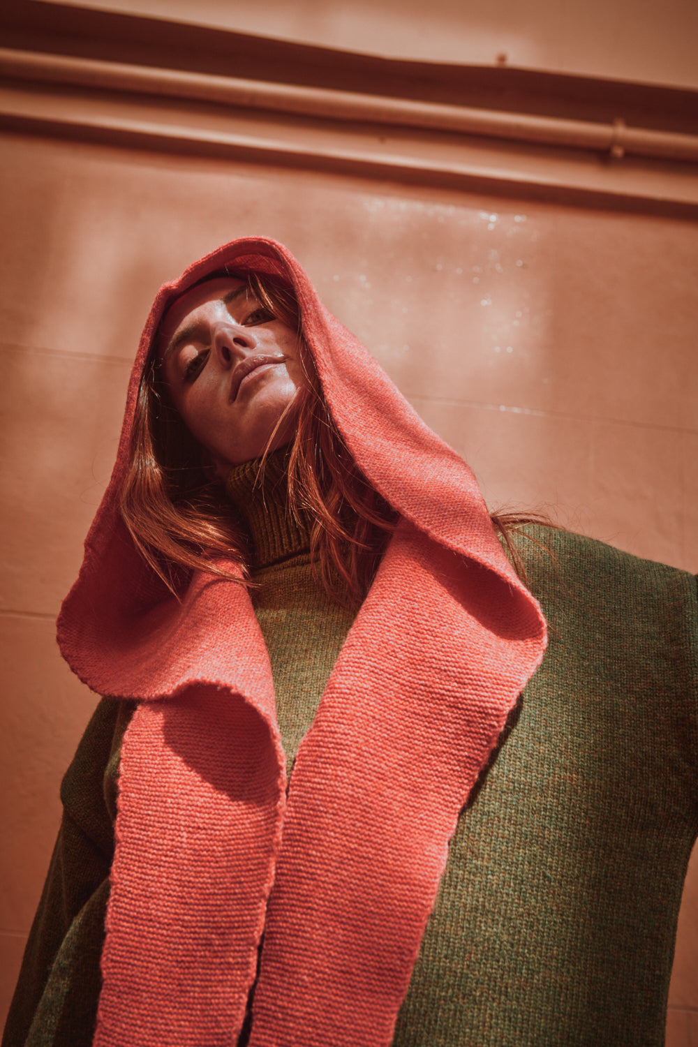 Person wearing a coral hooded garment against a brown background