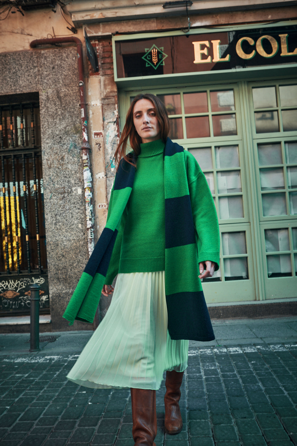 Woman wearing a green and navy scarf on a city street 