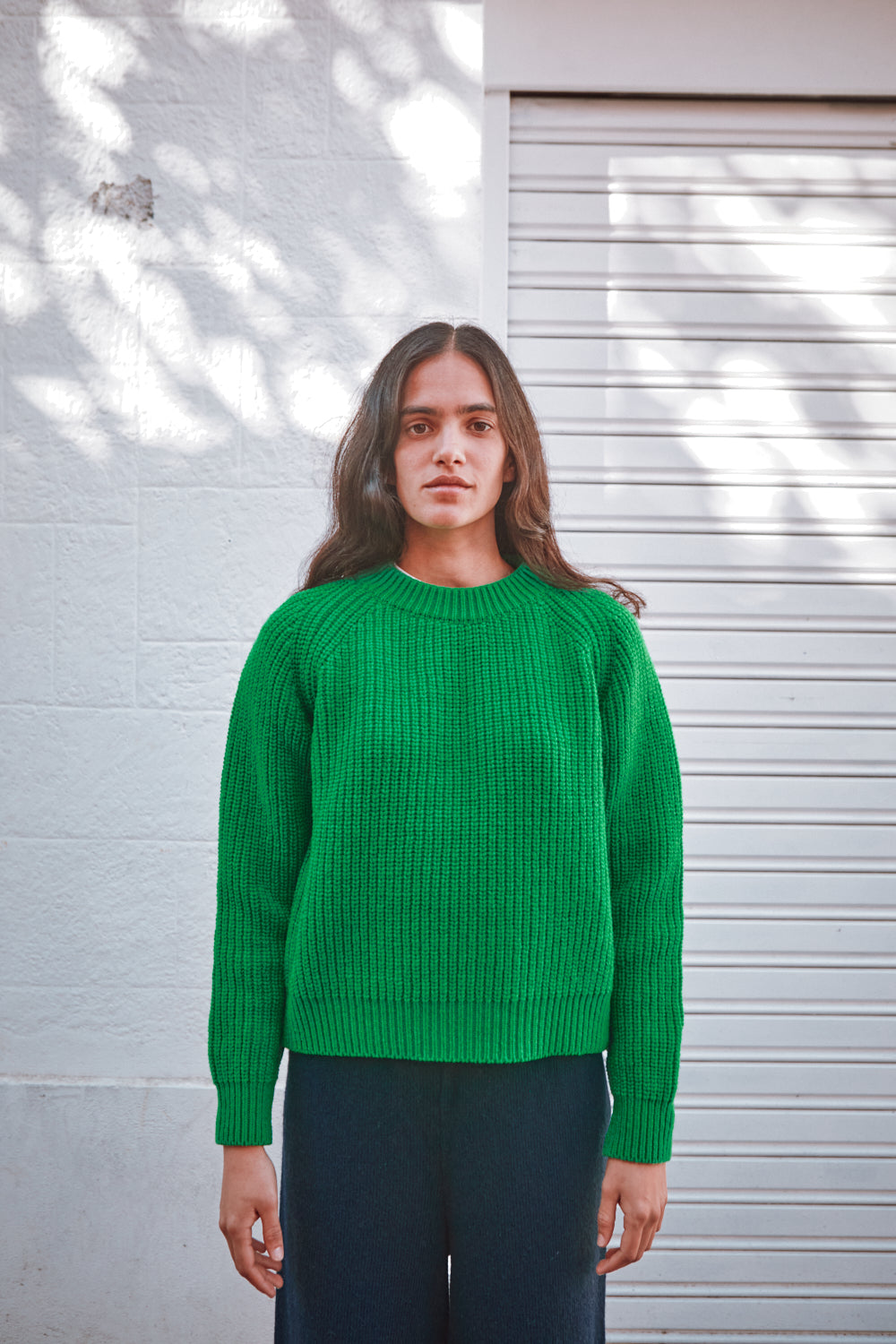 Personne portant un pull vert devant un mur blanc avec des ombres.