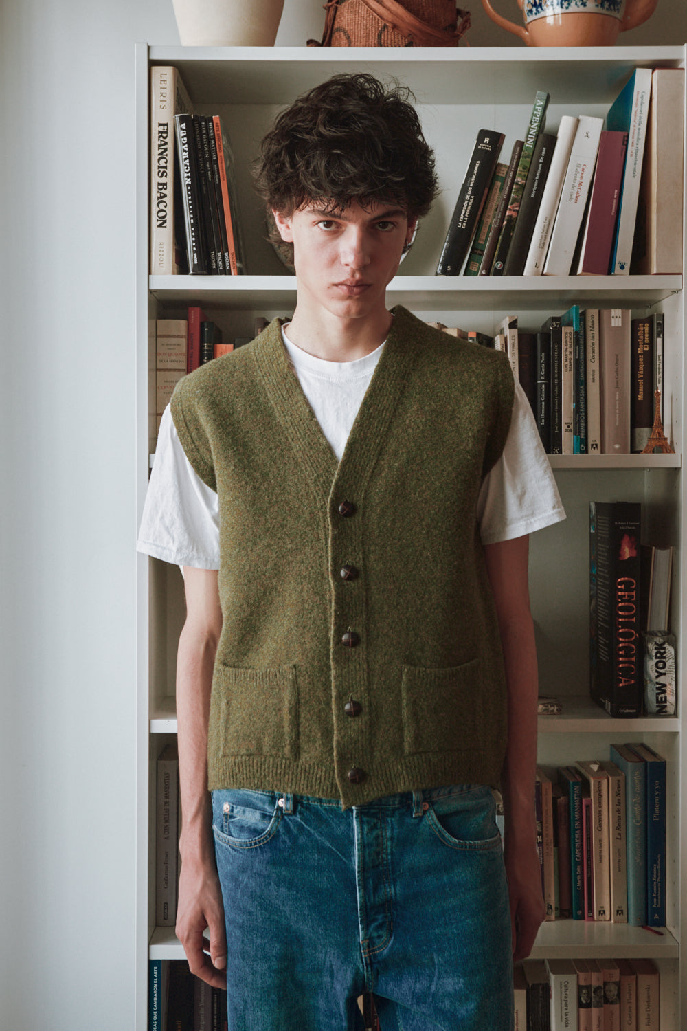 Personne portant un gilet vert sur une chemise blanche devant une étagère.