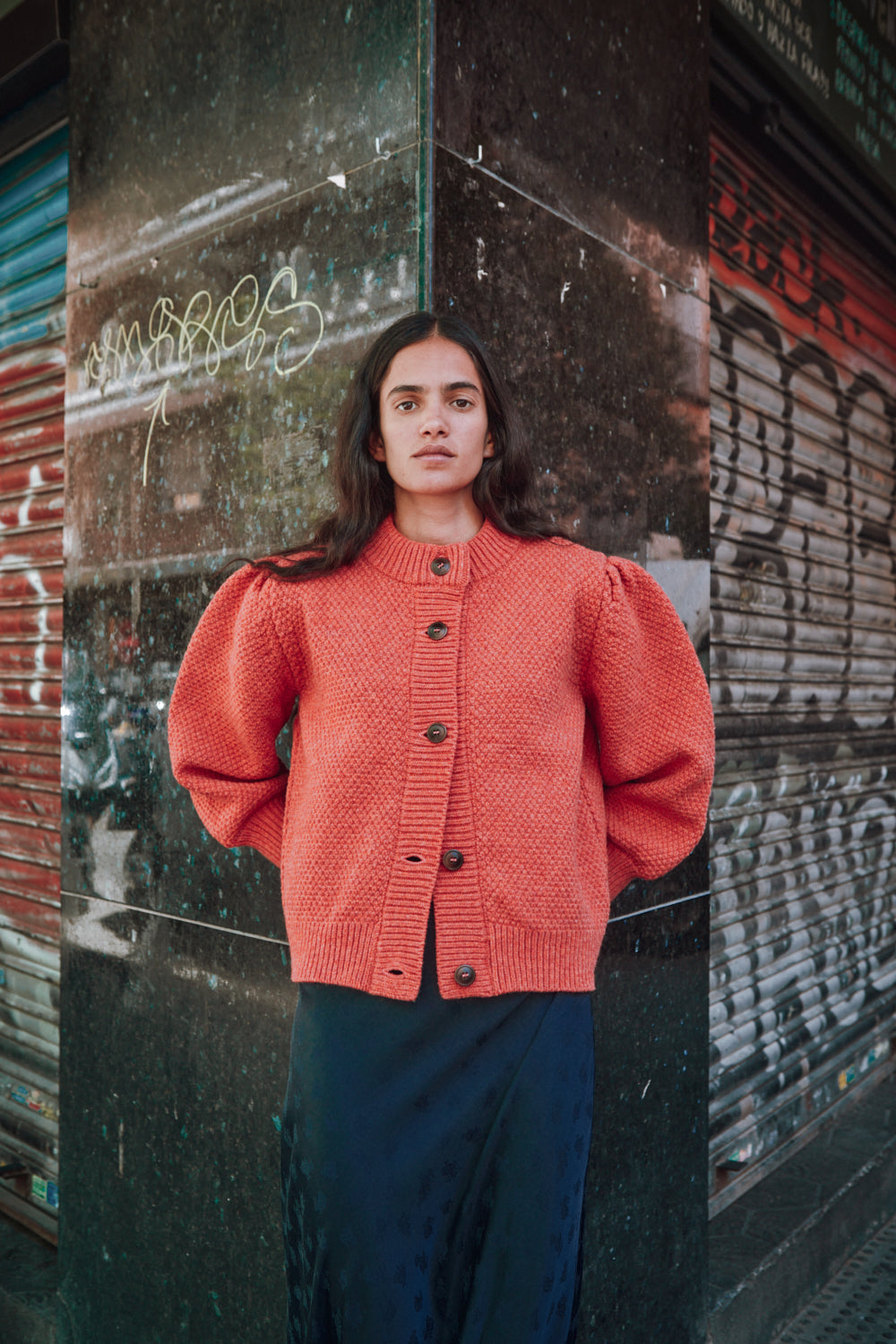Personne portant un gilet L'ENVERS en tricot rouge devant un mur texturé.