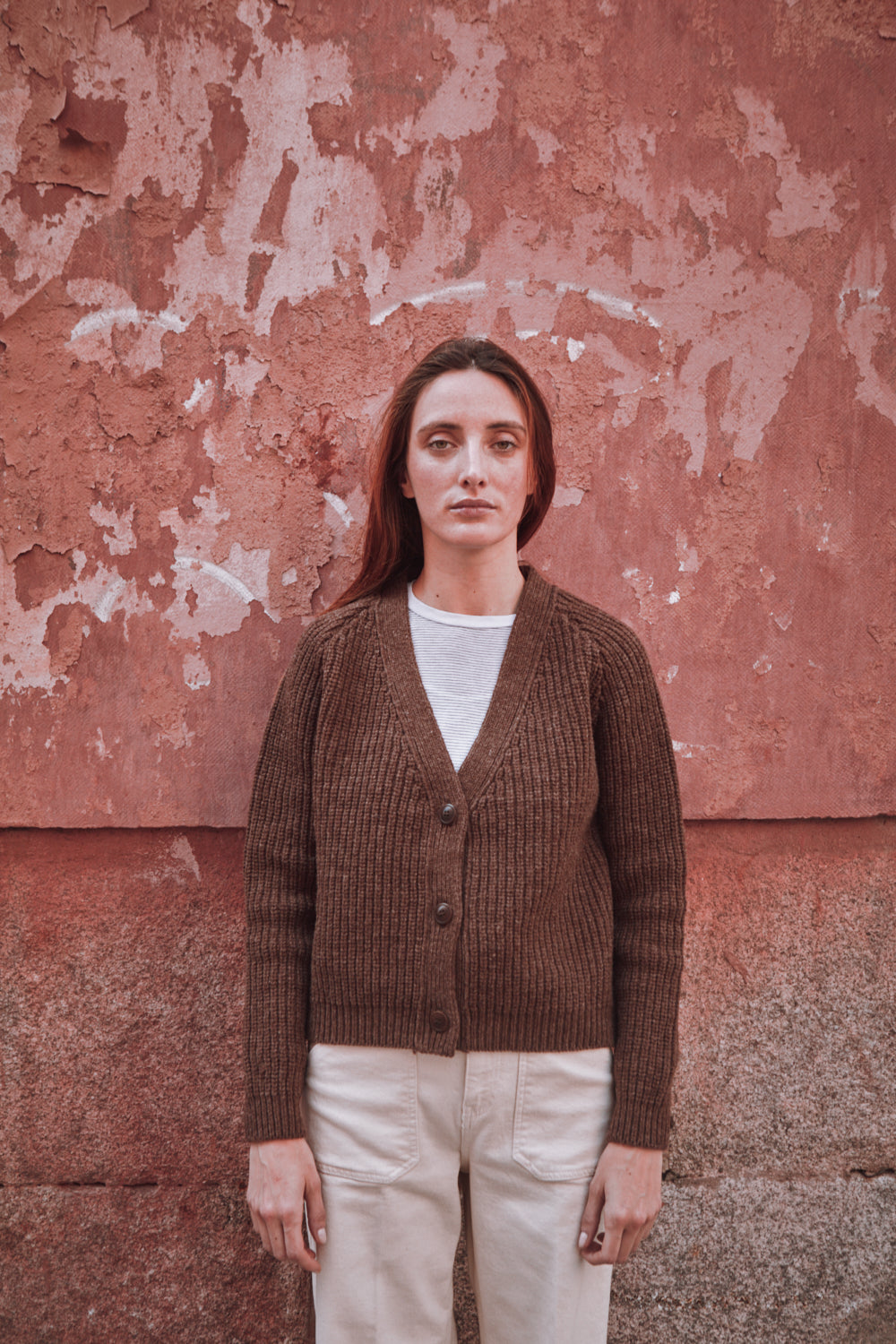Femme portant un gilet marron sur un mur rouge texturé