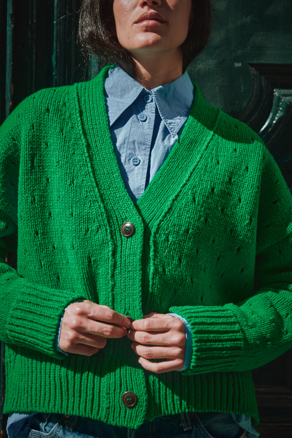 Personne portant un gilet tricoté vert sur une chemise bleu clair.