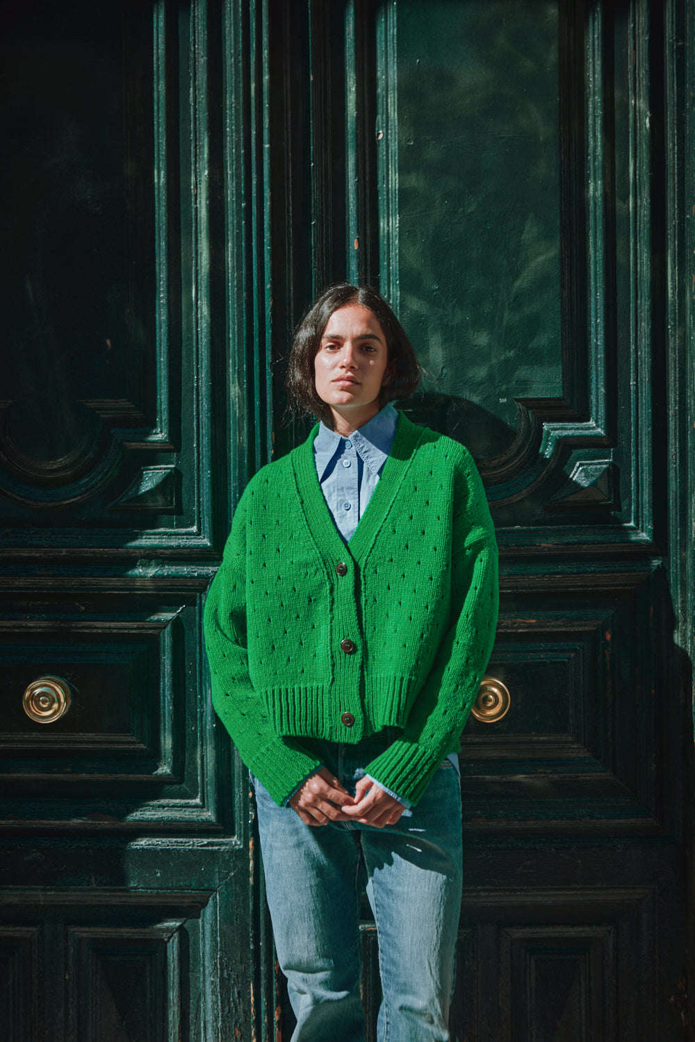 Personne portant un gilet vert devant une porte vert foncé.