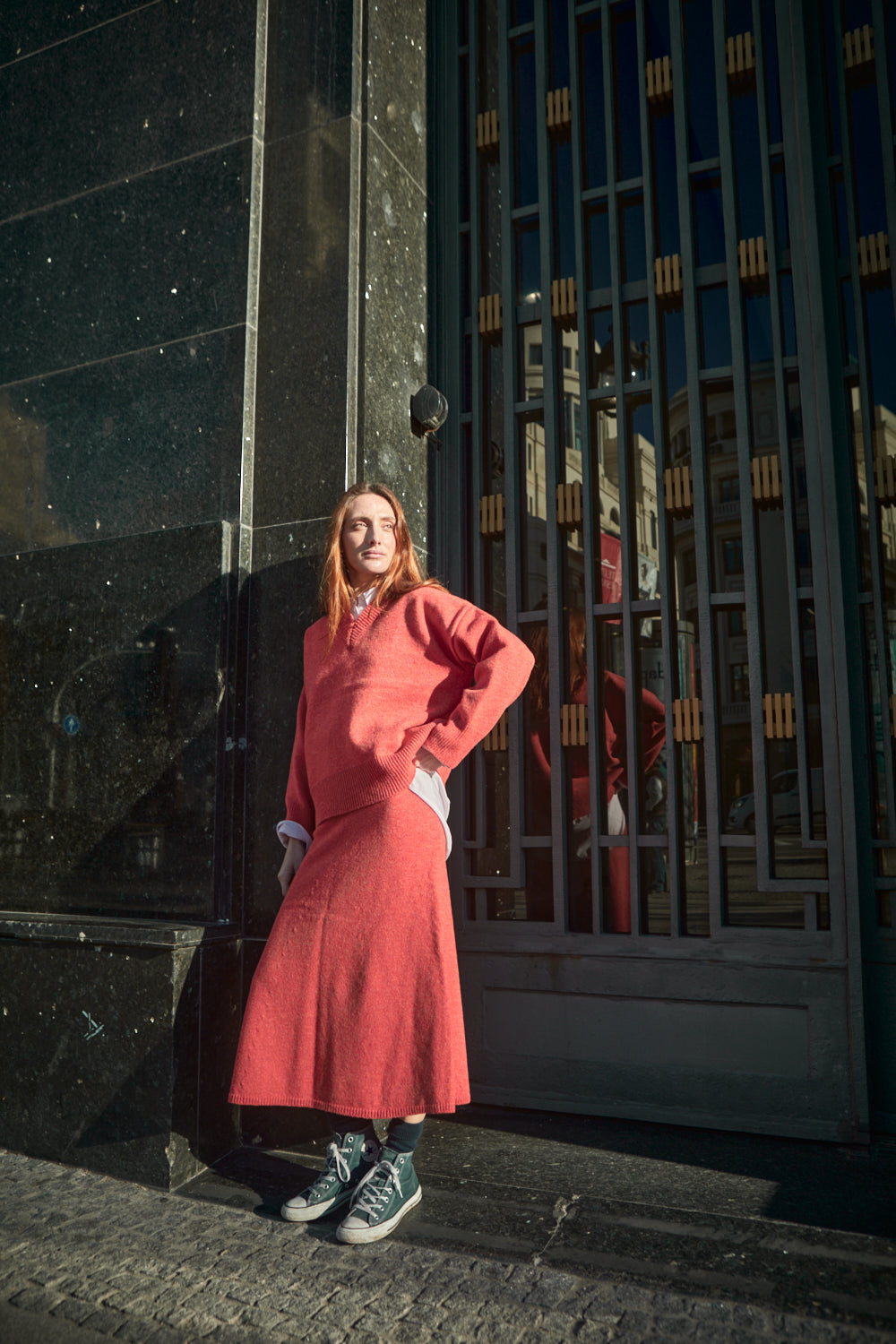 Personne portant une tenue corail devant un mur texturé.