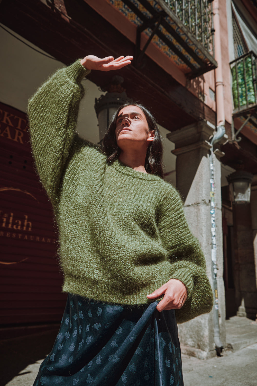Femme portant un pull vert pull L'ENVERS debout contre un mur texturé.