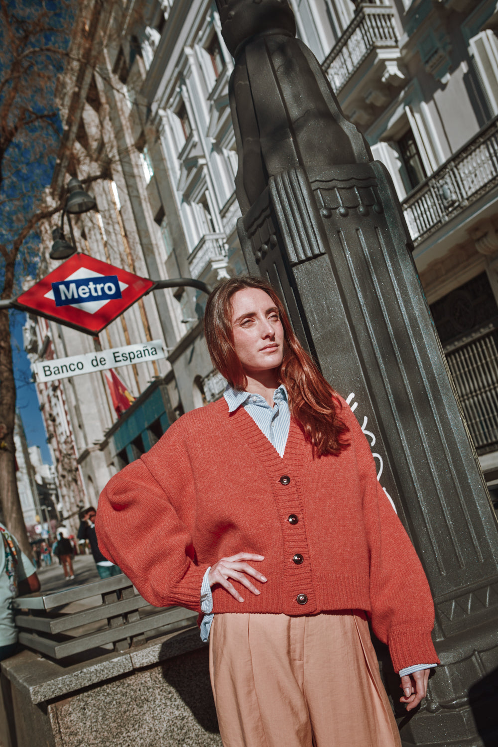 Femme vêtue d'un gilet orange dans une rue de la ville avec un panneau de métro en arrière-plan
