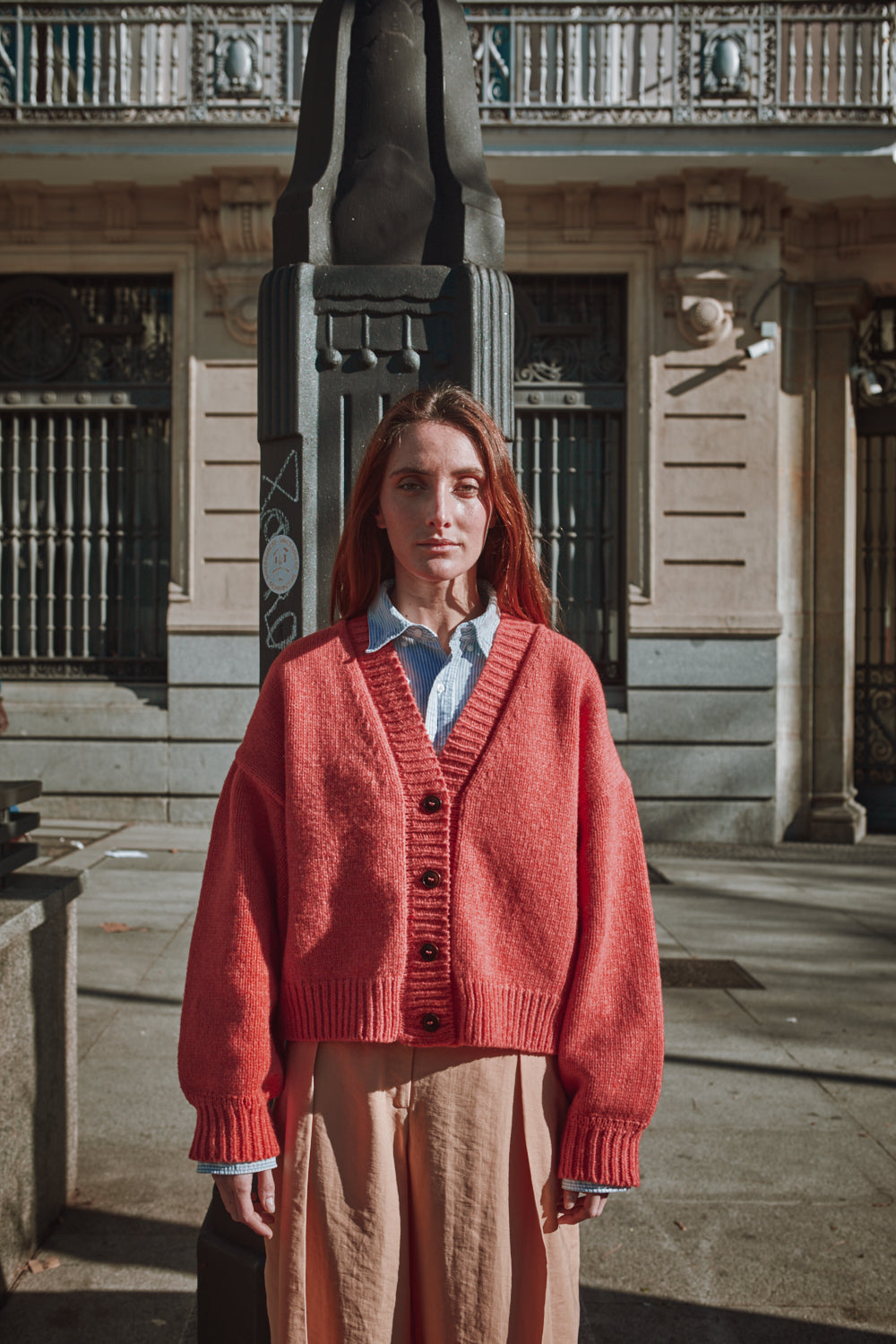 Femme portant un gilet rouge devant un bâtiment avec des détails architecturaux.