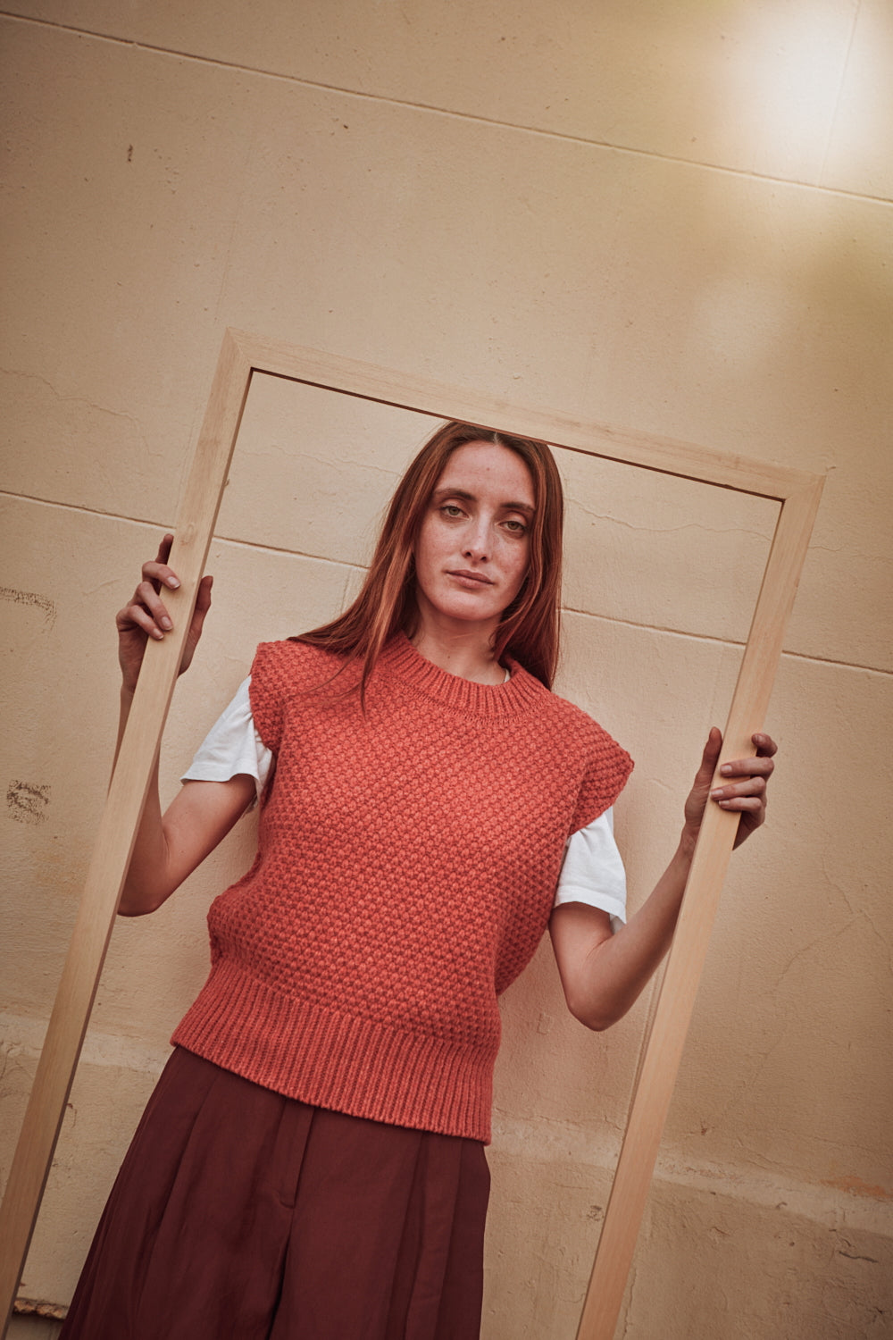 Femme portant un gilet en maille L'ENVERS corail sur une chemise blanche devant un mur beige.