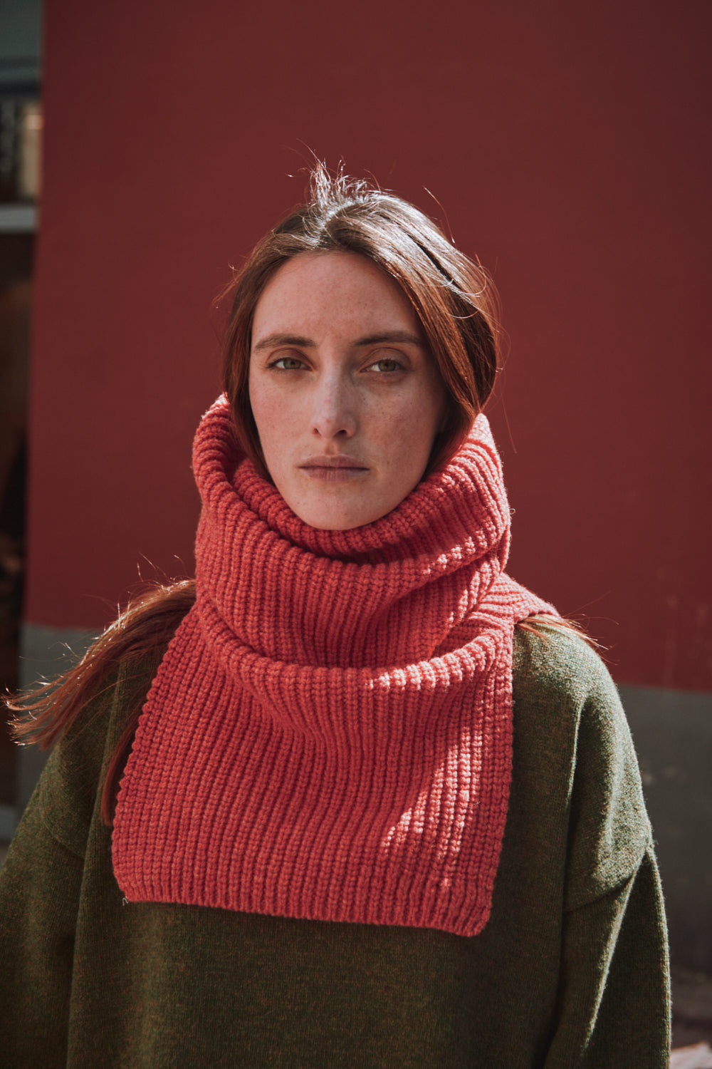 Personne portant une cagoule en tricot corail contre un mur rouge