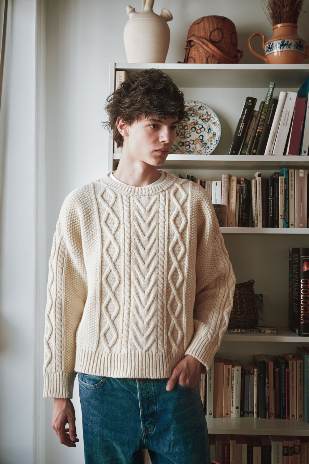 Personne portant une pull câble de couleur crème avec une bibliothèque en arrière-plan