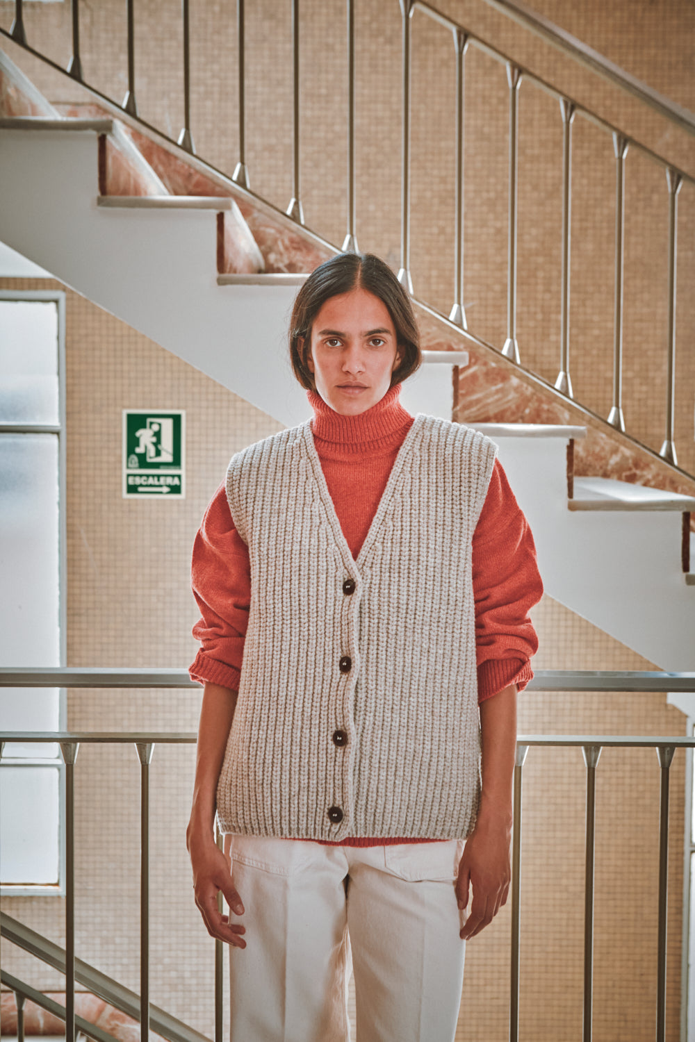 Personne portant un gilet à motifs sur un pull rouge dans un intérieur avec des escaliers.