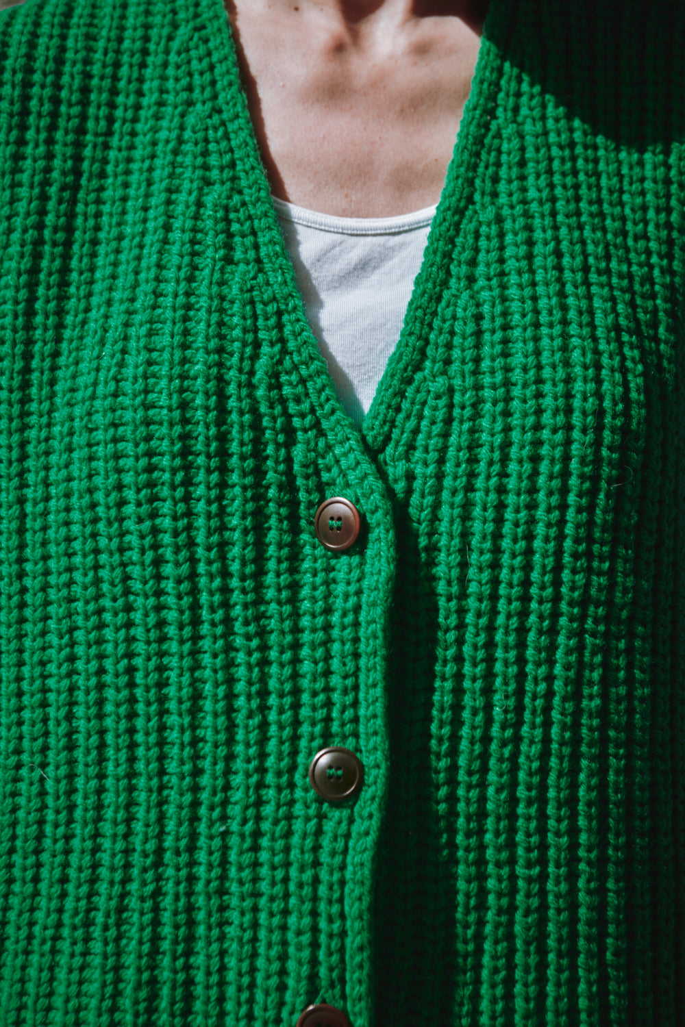gilet tricoté vert avec boutons sur une personne portant une chemise blanche.